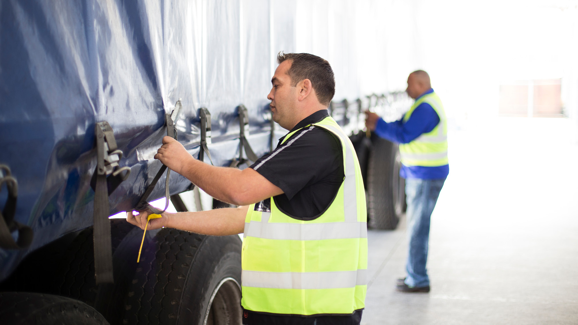 Two people securing a tarp over a load